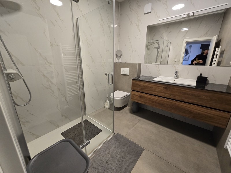 Przestronna łazienka z prysznicem, umywalką i eleganckimi płytkami.