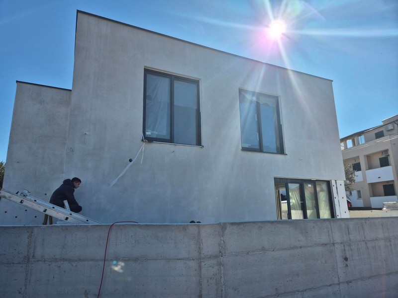 Widok zewnętrzny domu z dużymi oknami i światłem słonecznym