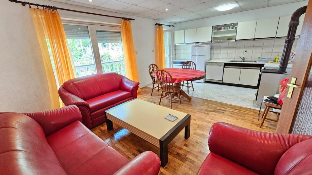 Część dzienna z czerwoną skórzaną sofą, wyjściem na balkon i otwartą kuchnią