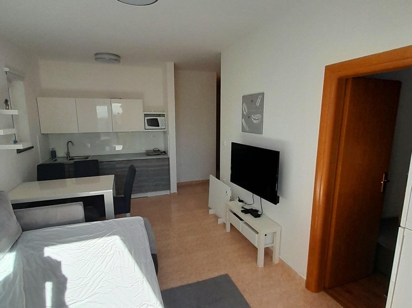 Pokój dzienny z telewizorem, stołem jadalnym i dostępem do sypialni