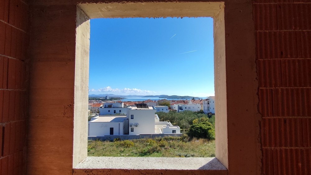 Widok przez niedokończone okna na morze i dzielnicę mieszkaniową