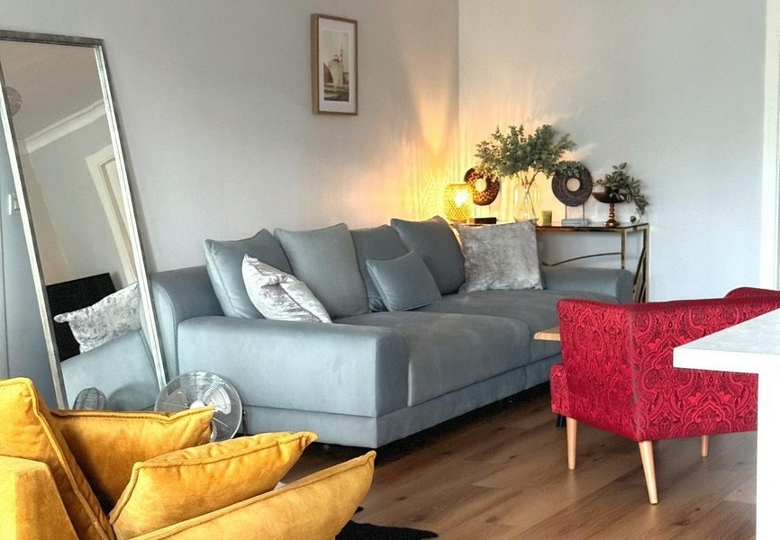 Część wypoczynkowa z dużym lustrem i szarą sofą