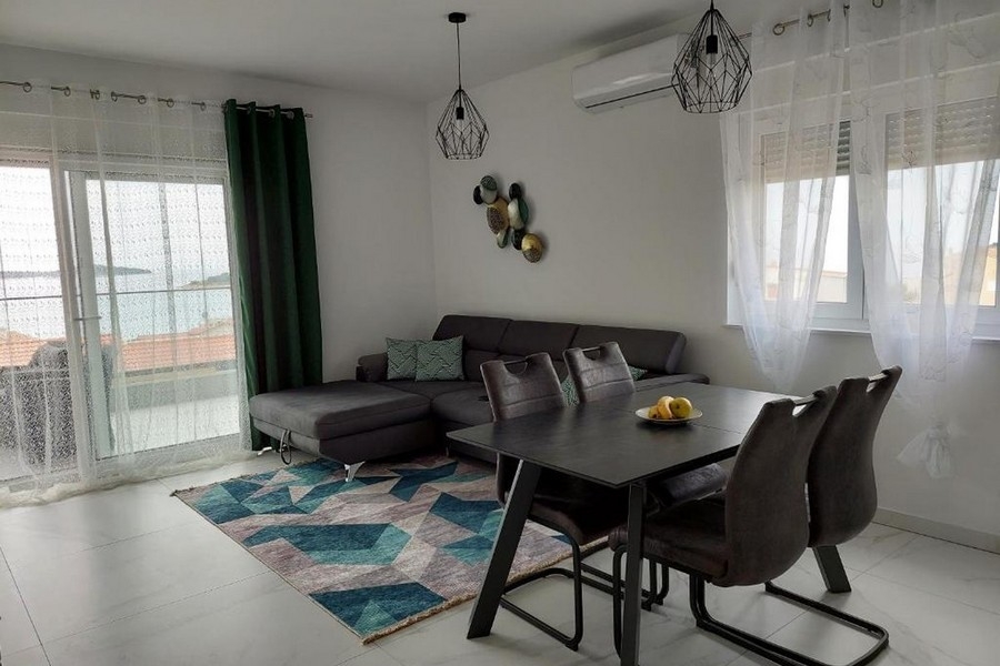 Pokój dzienny z sofą, stołem jadalnym i widokiem na morze przez duże okno z przodu