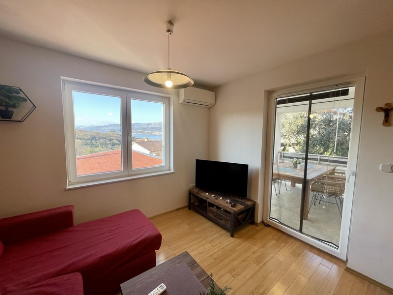 Pokój dzienny z sofą, telewizorem i wyjściem na balkon z widokiem na morze