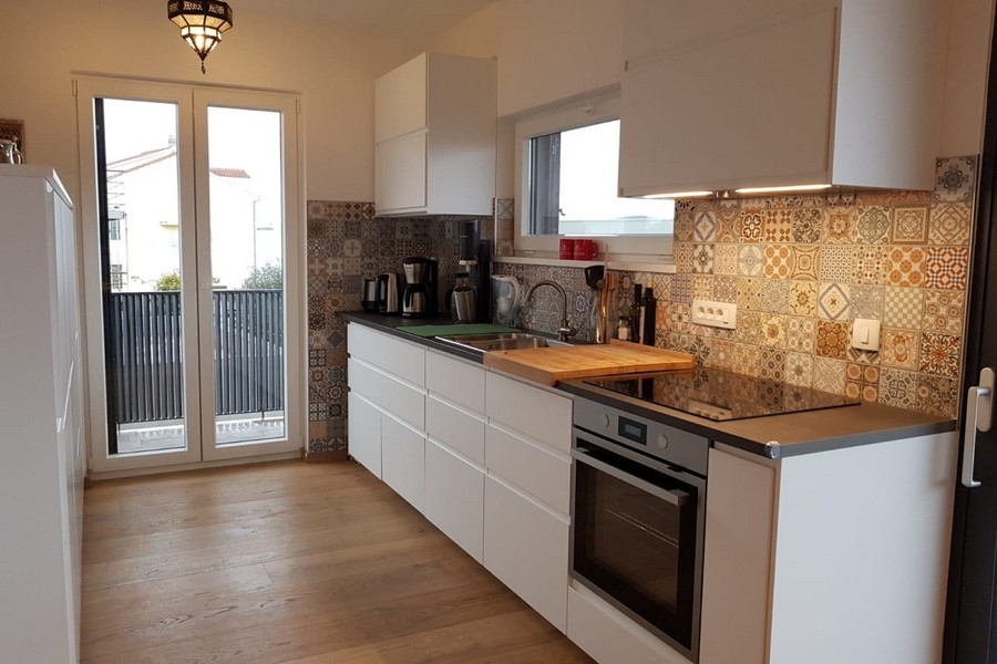 Nowoczesna kuchnia z zabudowanym sprzętem AGD i ozdobną tylną ścianą wyłożoną kafelkami