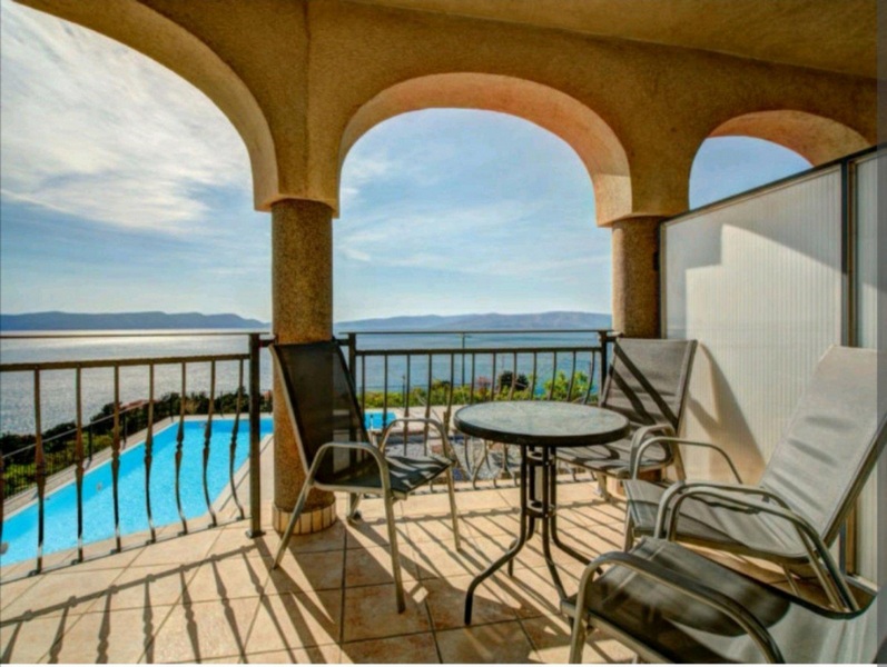 Widok na basen i morze z zadaszonego tarasu na piętrze.