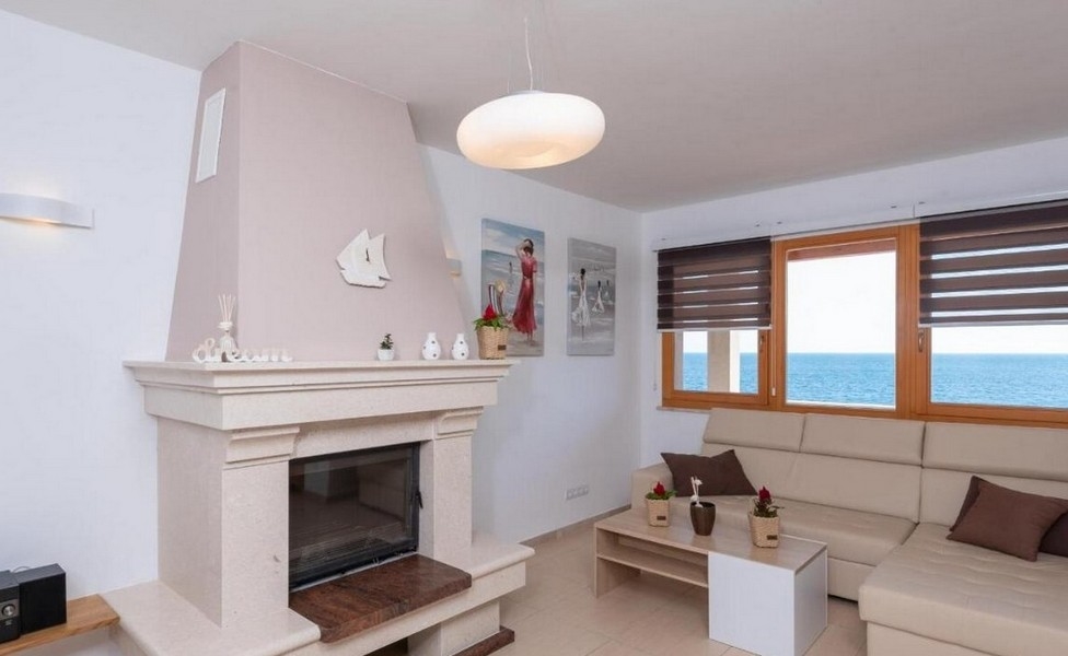 Kominek w salonie z widokiem na morze i jasną kanapą.