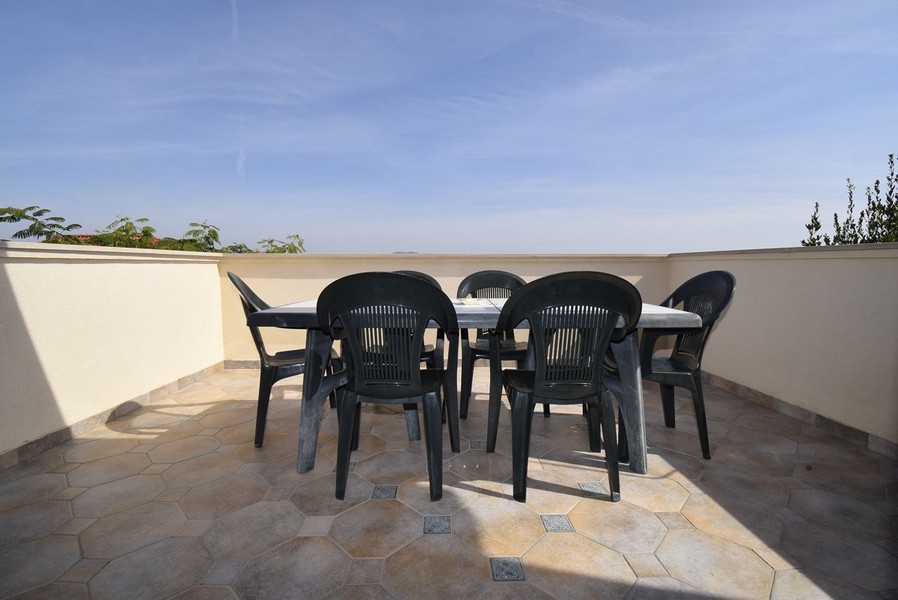 Przestronny, otwarty taras z prostymi krzesłami ogrodowymi.