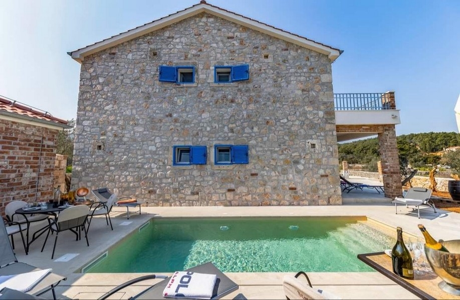 Widok z tyłu chorwackiej kamiennej willi na sprzedaż z prywatnym basenem i miejscem do grillowania.