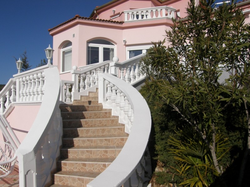 Widok z przodu różowej willi w Chorwacji z krętymi białymi schodami i śródziemnomorską roślinnością