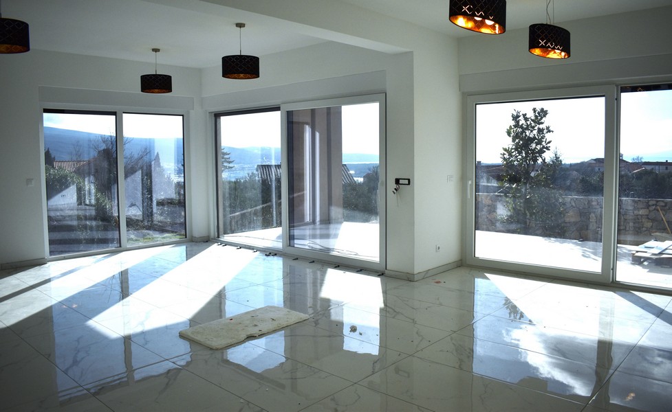 Jasny, nasłoneczniony salon w willi na Krku z dużymi oknami i widokiem na morze.