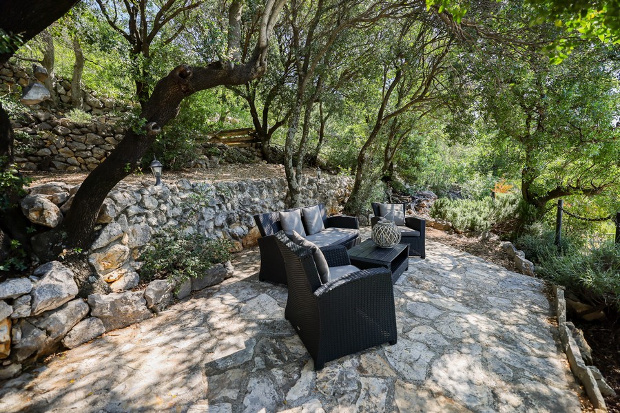 Na sprzedaż zewnętrzna część wypoczynkowa kamiennego domu w Chorwacji, otoczona drzewami i murami z kamienia naturalnego.