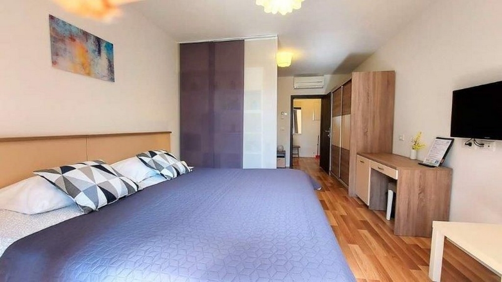 Sypialnia w jednym z trzech apartamentów w domu na sprzedaż na Istrii, z dużym łóżkiem, szafą i telewizorem.