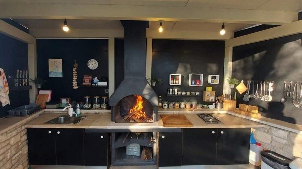 Na sprzedaż kuchnia z kominkiem do grillowania w domu z trzema apartamentami na Istrii, z czarnymi blatami roboczymi i nowoczesnymi urządzeniami kuchennymi.