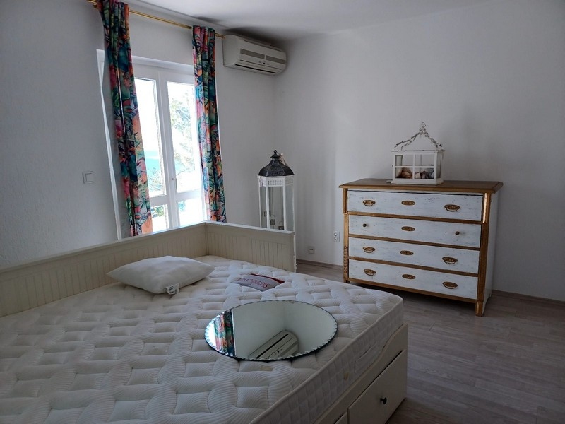 Sypialnia z podwójnym łóżkiem i białą komodą w willi na sprzedaż na wyspie Cres w Chorwacji, z widokiem na przyrodę