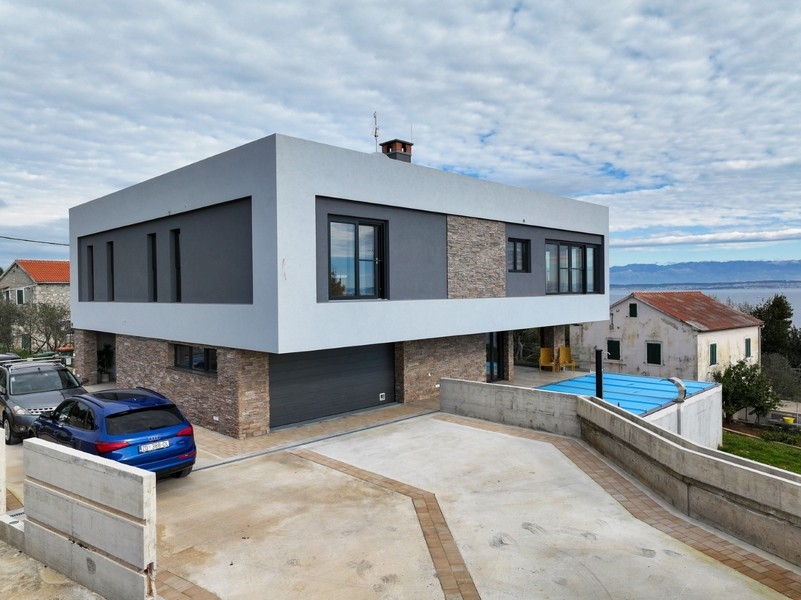 Widok z przodu współczesnej willi z garażem na sprzedaż w Ugljan w Chorwacji, otoczonej utwardzonym podjazdem i częściowym widokiem na morze