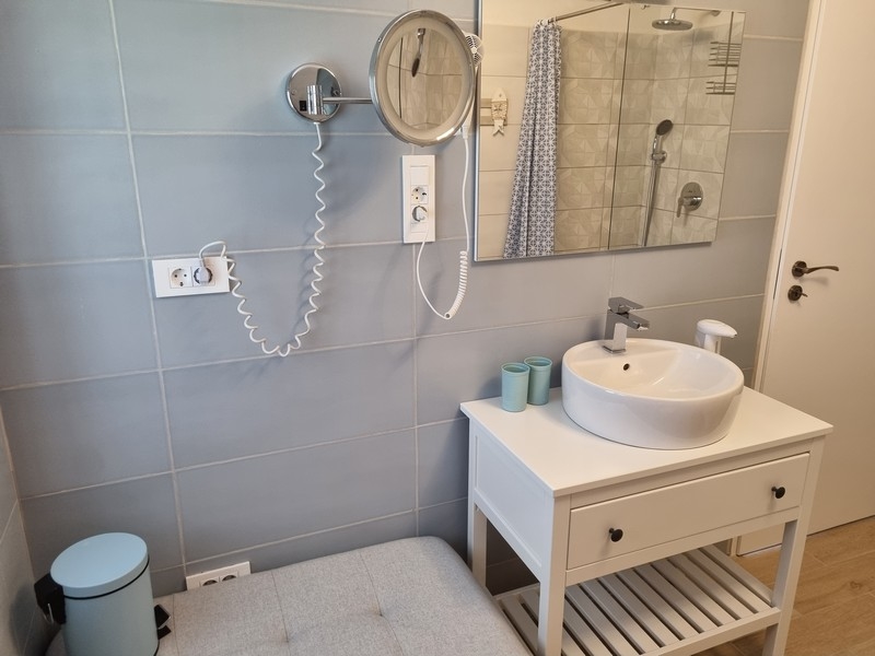 Łazienka w nadmorskim apartamentowcu na sprzedaż w Karlobag w Chorwacji, z jasnoniebieskimi kafelkami, białą konsolą toaletkową, lustrem i wieszakiem na ręczniki