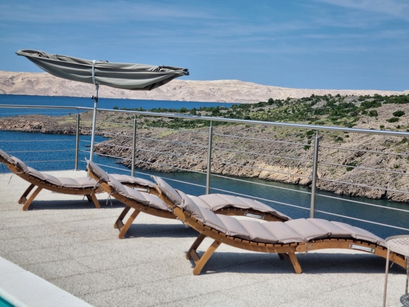 Strefa relaksu z leżakami i parasolem na tarasie apartamentowca w Karlobag w Chorwacji, z widokiem na morze.