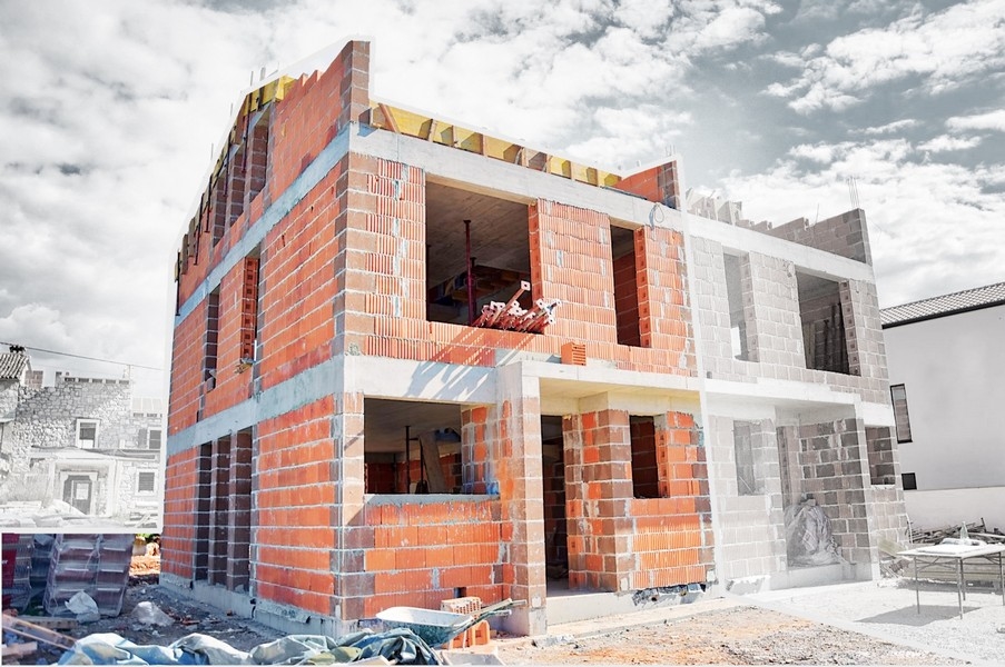 Półwykończony dom bliźniaczy w fazie budowy z widocznymi ceglanymi ścianami i otworami na okna i drzwi