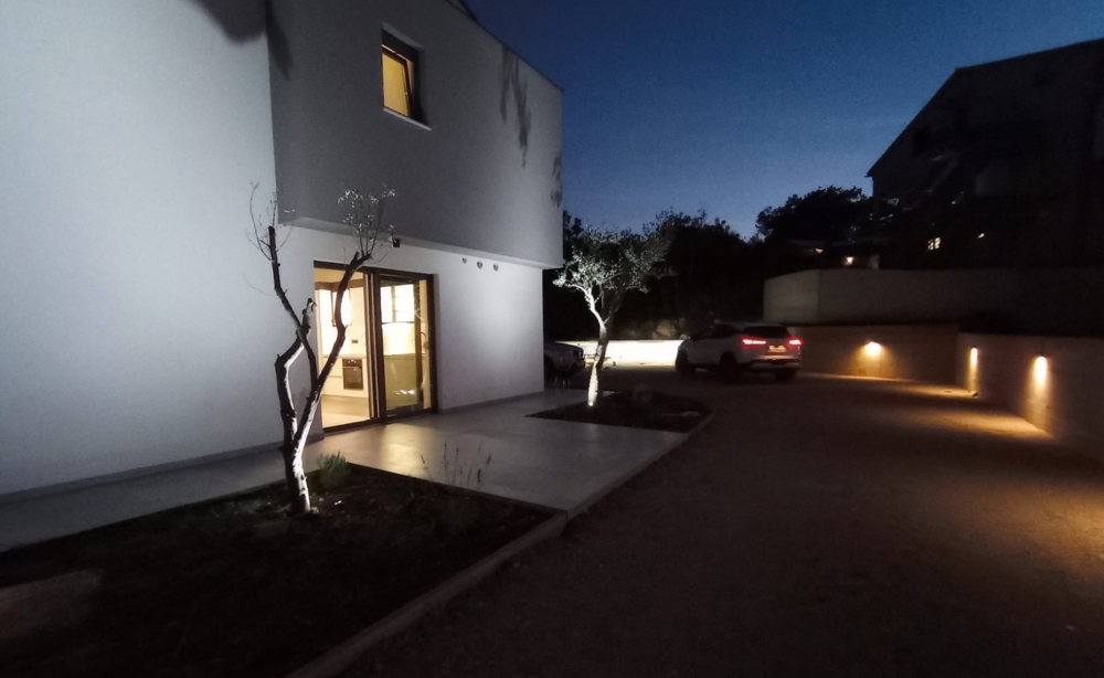 Nocne zdjęcie nieruchomości w Chorwacji z oświetleniem zewnętrznym i samochodem zaparkowanym na podwórzu.