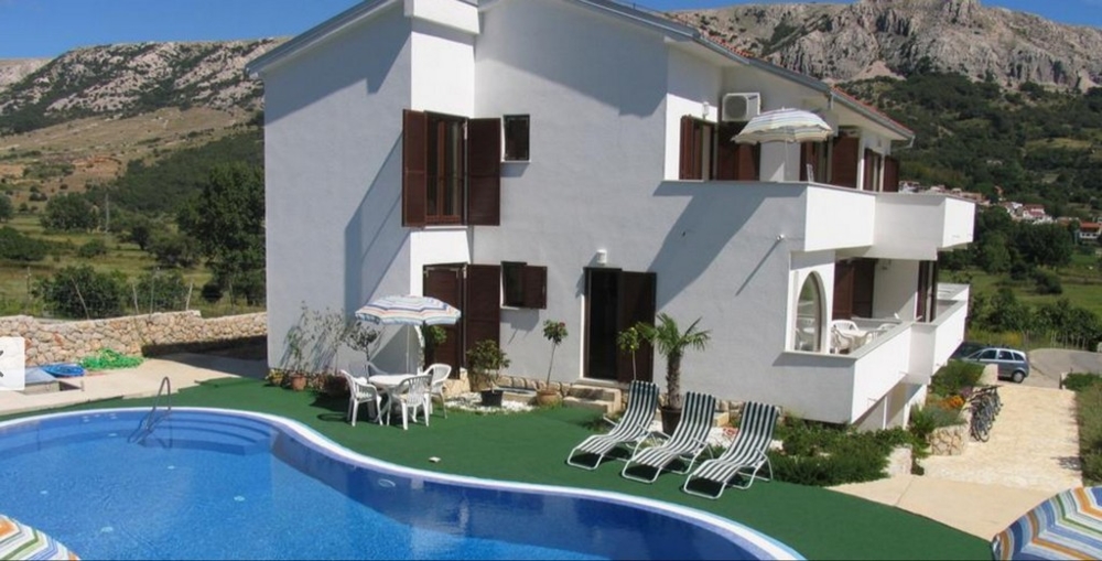 Domek letniskowy w Chorwacji z niebieskim basenem i leżakami przed górzystym krajobrazem, nieruchomości w Chorwacji