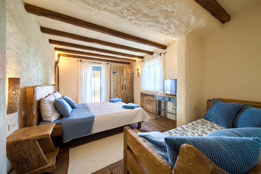 Przytulna sypialnia z rustykalnymi drewnianymi meblami i naturalnym oświetleniem, przyjazny aspekt posiadłości na wyspie Krk.