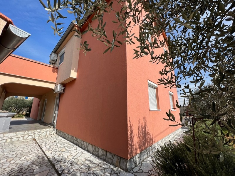 Nieruchomości Chorwacja, miasto Krk, wyspa Krk Kupno budynku mieszkalnego, widok z bliska na bok domu z oknami i drzewem oliwnym na pierwszym planie