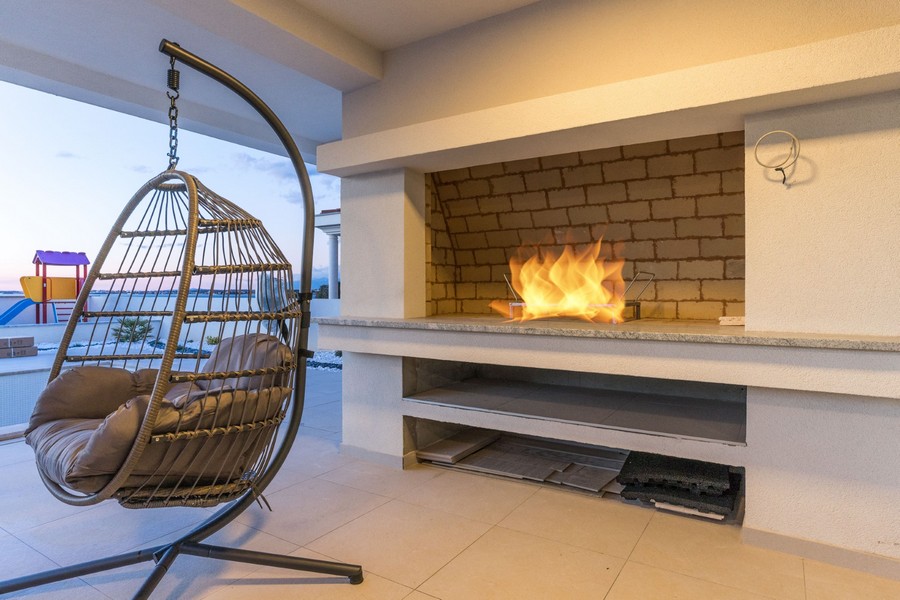 Nowoczesna luksusowa willa z wiszącym krzesłem i wbudowanym kominkiem, idealna na przytulny wieczór w Twojej nowej nieruchomości w Chorwacji.