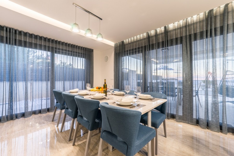 Elegancka jadalnia z dużymi oknami zapewniającymi naturalne światło i widok na wymarzoną posiadłość w Chorwacji.