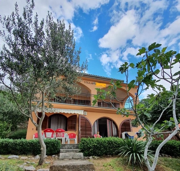 Wygląd zewnętrzny dwupiętrowej willi z pomarańczową fasadą i łukowatymi oknami otoczonej drzewami i terenami zielonymi