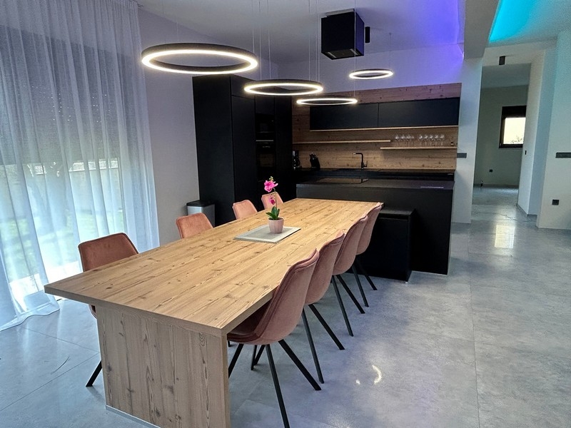 Nowoczesna kuchnia i jadalnia willi ze stylowym oświetleniem i drewnianym stołem