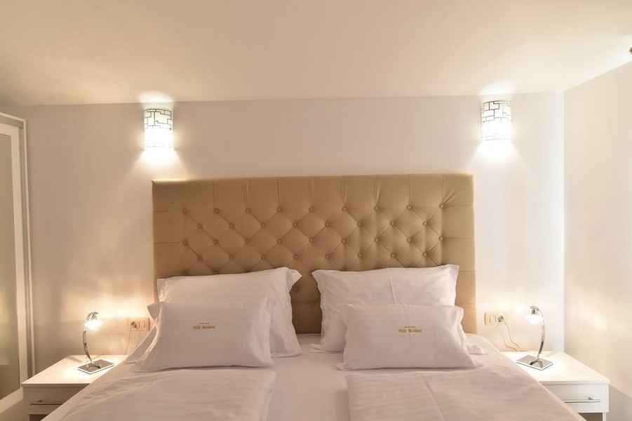 Zbliżenie na łóżko w sypialni z nowoczesnym oświetleniem, oferowane przez agencję nieruchomości Panorama Scouting