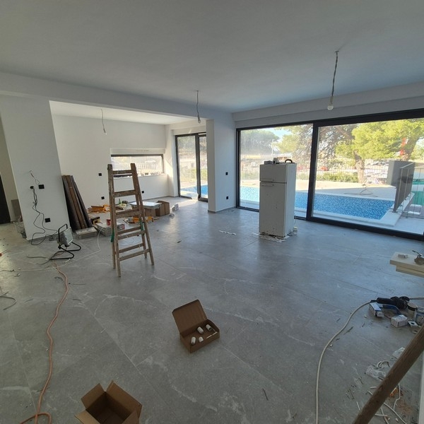 Nowoczesna dwupiętrowa willa z dużymi oknami, balkonami i podwójnym garażem, z eleganckim samochodem przed domem, położona w Drage w Chorwacji.