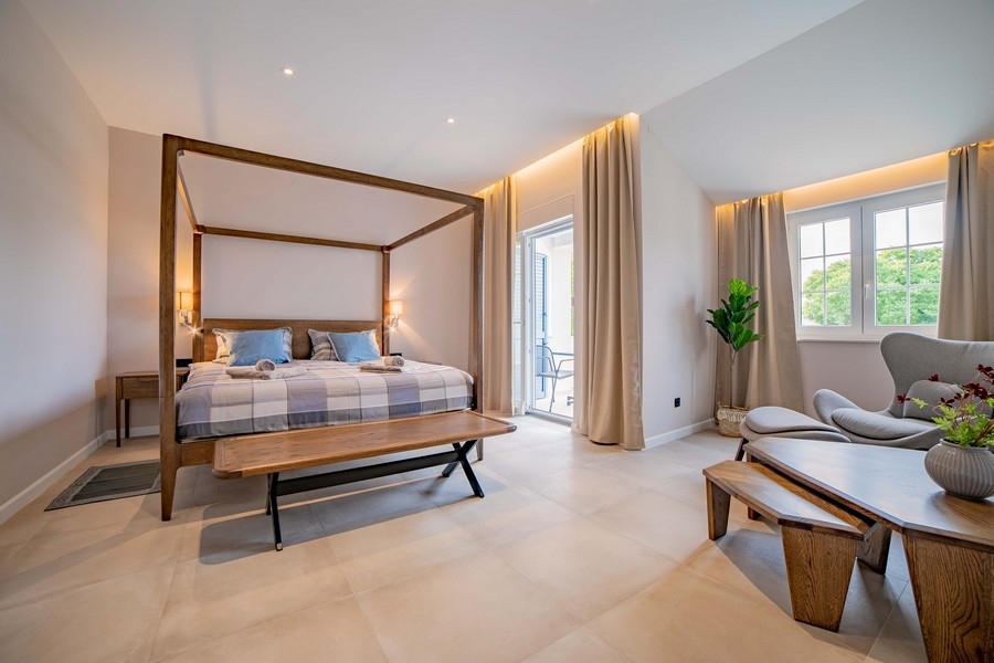 Przestronna sypialnia z łóżkiem z baldachimem, ławką i wygodnymi siedziskami, urządzona w jasnych kolorach i z dużą ilością naturalnego światła
