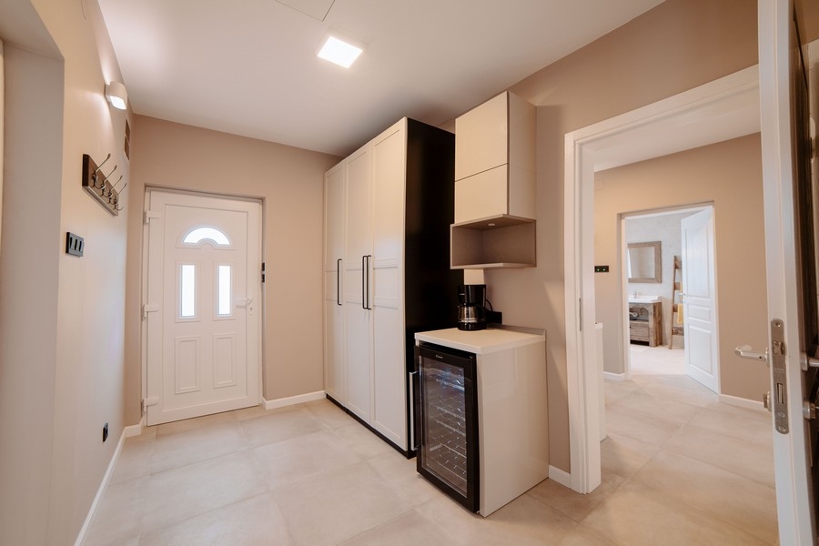 Strefa wejściowa z nowoczesnymi szafkami, chłodziarką do wina i widokiem na stylową łazienkę