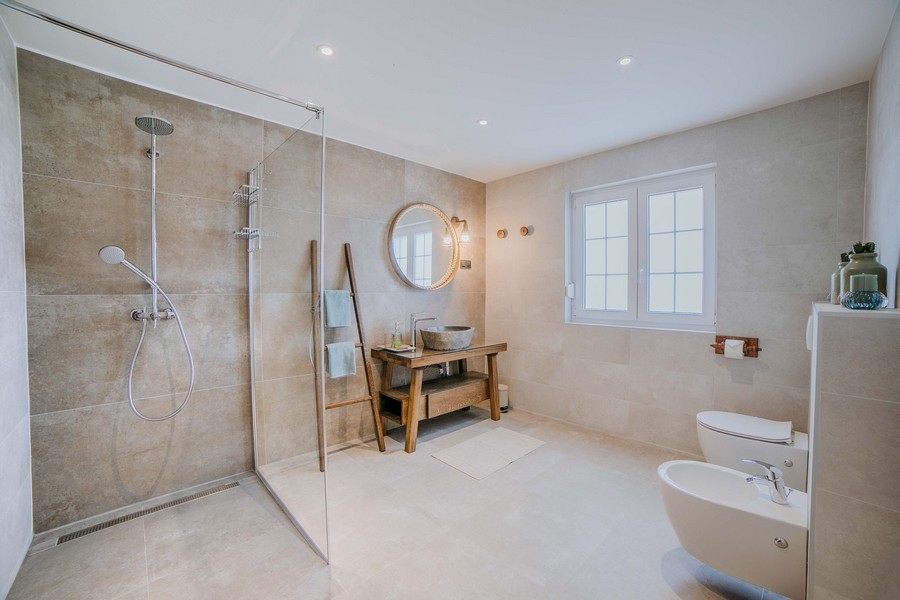 Luksusowa łazienka z dużą kabiną prysznicową, bidetem i rustykalną drewnianą toaletką, zaprojektowana w kolorach ziemi i nowoczesnym wyposażeniu