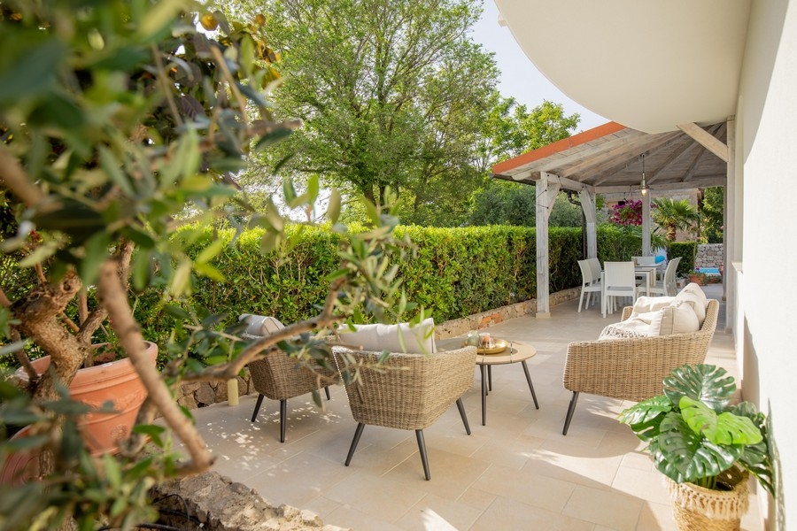 Część wypoczynkowa na świeżym powietrzu z meblami wiklinowymi i zacienioną jadalnią otoczoną zielenią i drzewami