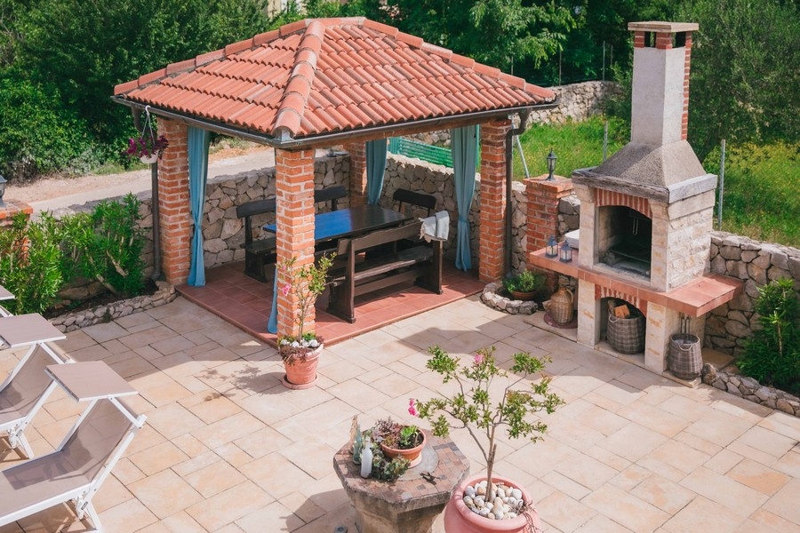 Miejsce do grillowania na świeżym powietrzu z ceglaną altaną, drewnianym stołem jadalnym i kamiennym piekarnikiem na tarasie wyłożonym kafelkami