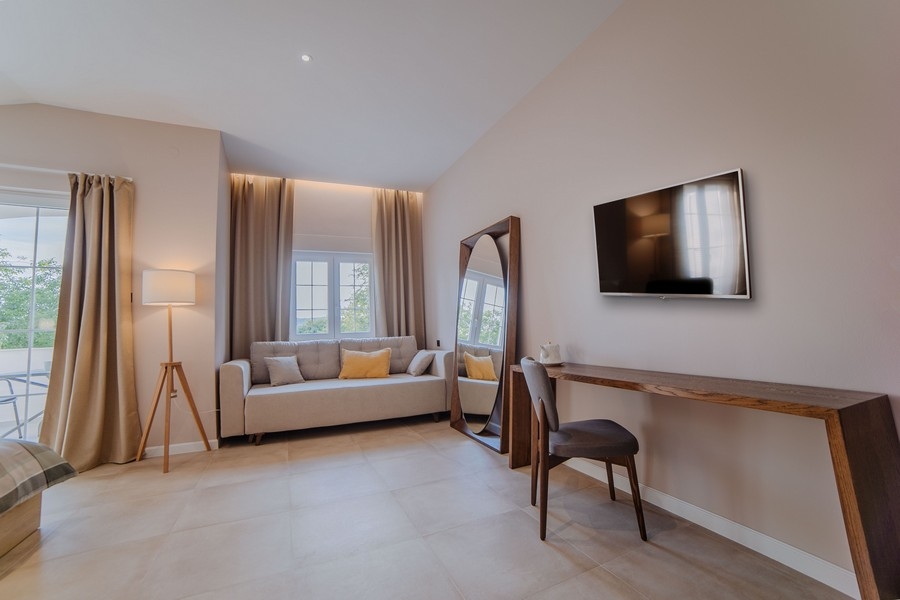 Przytulny salon z kilkoma sofami, telewizorem i dużymi oknami z niebieskimi zasłonami, które wpuszczają naturalne światło