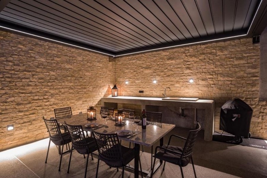 Zadaszony teren zewnętrzny z jadalnią i grillem, otoczony kamiennymi ścianami