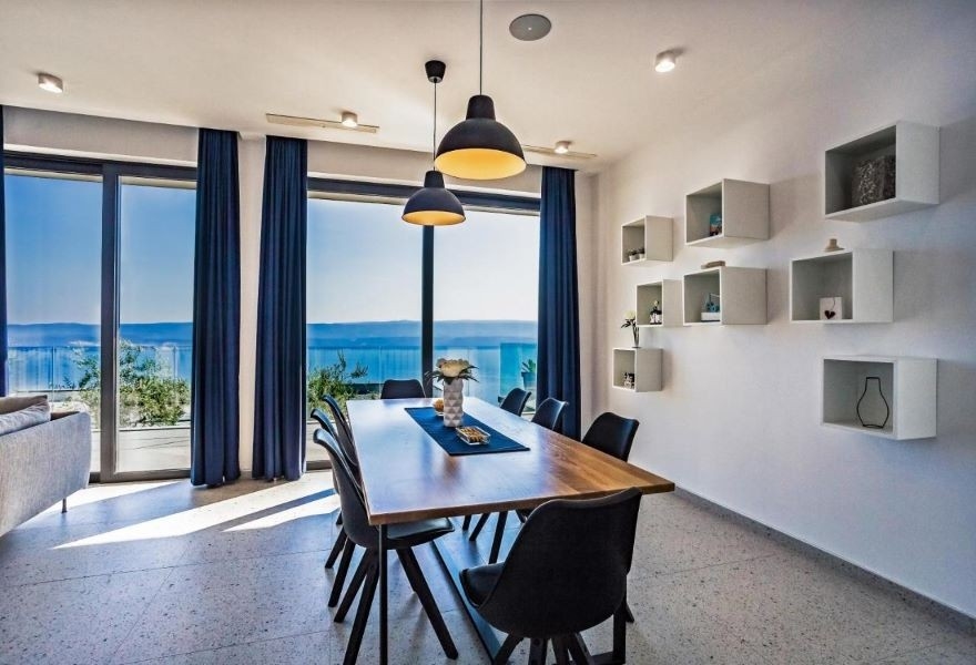 Jadalnia z nowoczesnym drewnianym stołem, czarnymi krzesłami i panoramicznym widokiem na morze