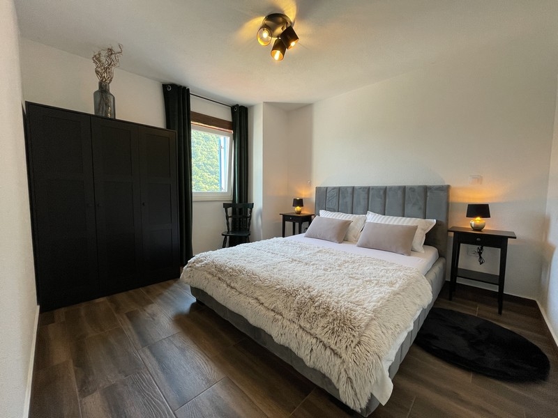 Sypialnia z szarym łóżkiem, czarną szafą i dwoma stolikami nocnymi oświetlonymi ciepłym światłem