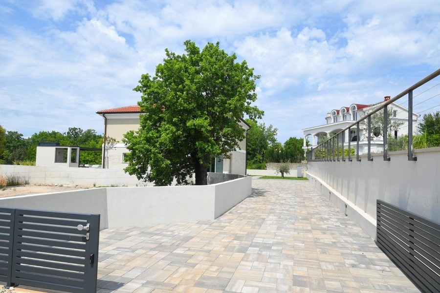 Duży utwardzony teren zewnętrzny z drzewem i nowoczesnym ogrodzeniem