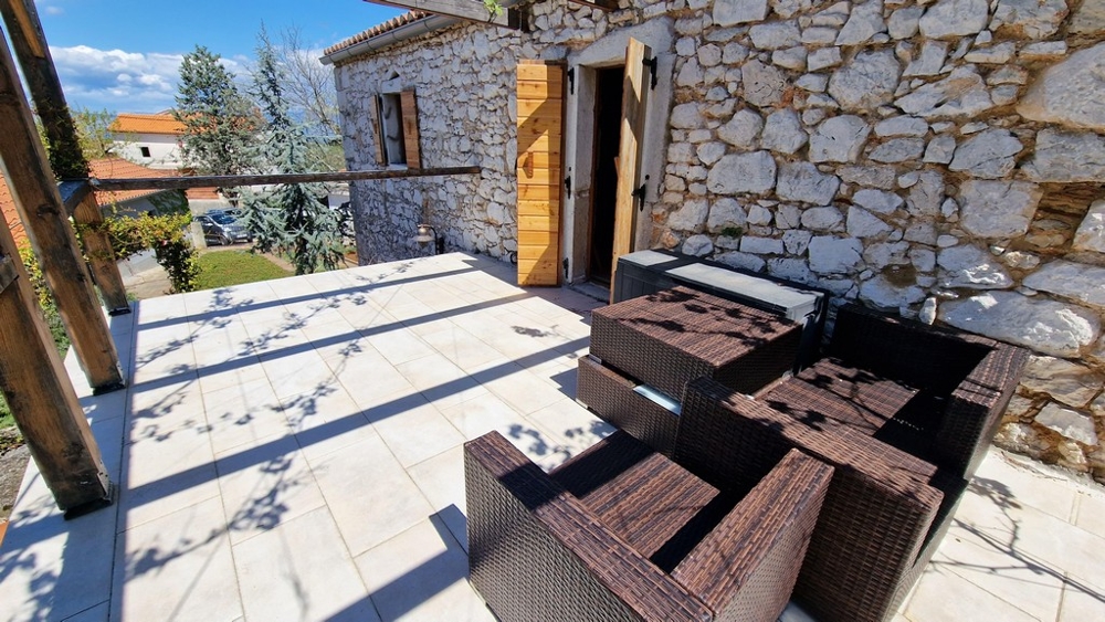 Taras słoneczny z miejscami do siedzenia przed rustykalnym kamiennym domem.