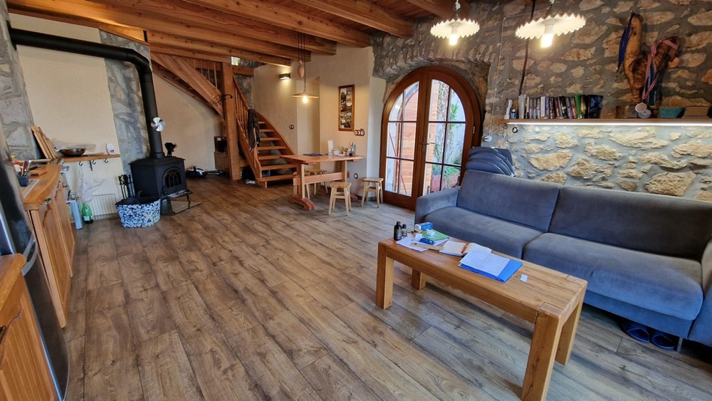 Salon na otwartym planie z odsłoniętymi belkami stropowymi, piecem opalanym drewnem i rustykalnym wnętrzem.