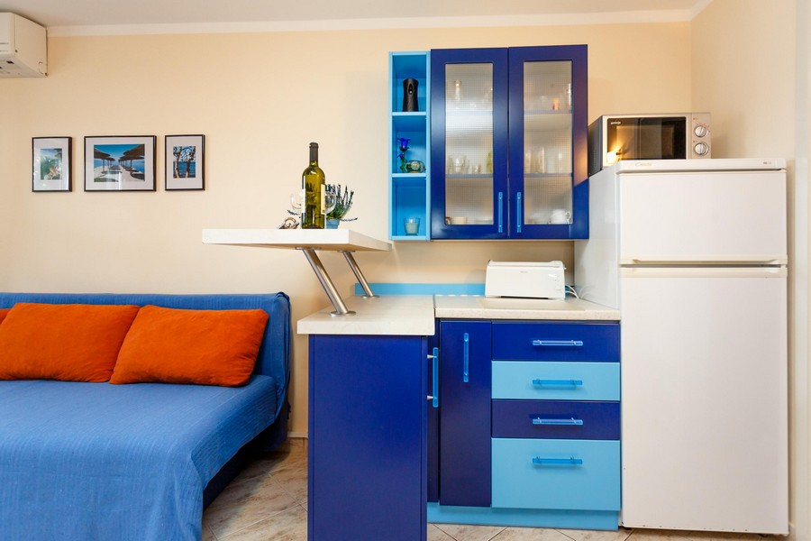 Kuchnia z niebieskimi szafkami, białą lodówką i małymi przyborami kuchennymi