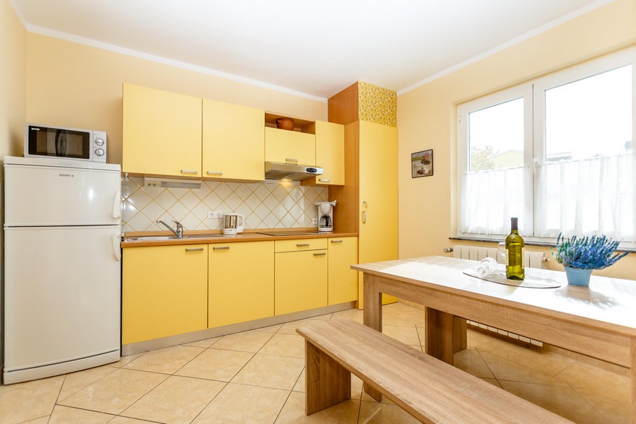 Żółta kuchnia ze stołem i ławami, jasne płytki na ścianach