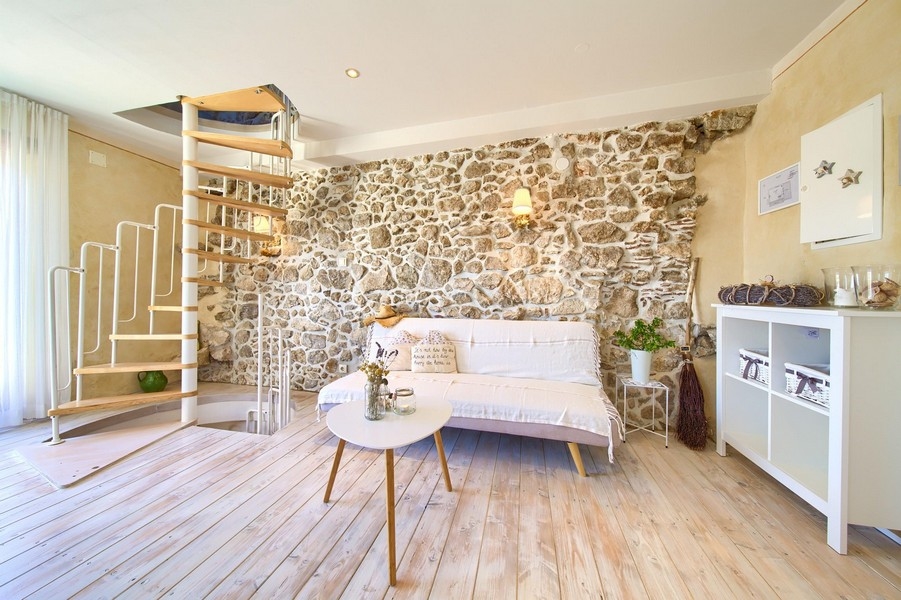 Przytulny salon z odsłoniętymi kamiennymi ścianami, sofą i kręconymi schodami prowadzącymi na górę.