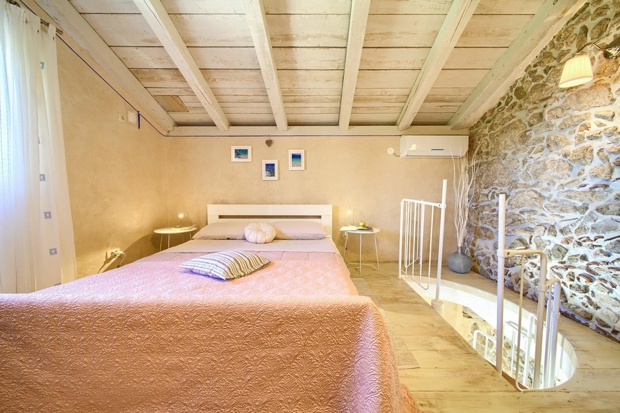 Sypialnia z drewnianymi belkami stropowymi i rustykalnymi meblami, do której prowadzą kręcone schody.