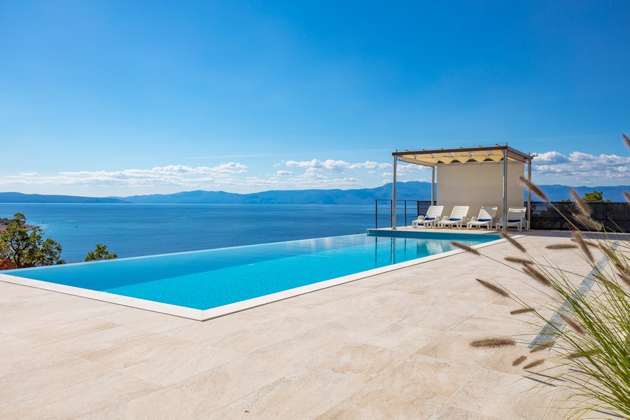 Basen bez krawędzi z leżakami, bezpośrednim widokiem na morze i błękitne niebo.